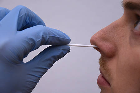 Eine medizinische Fachangestellte nimmt mit einem Wattestäblichen einen Abstrich in der Nase eines jungen Mannes