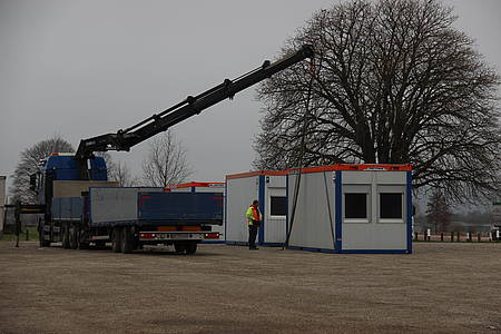 Ein Büro-Container wird von einem Kran neben einem Zelt abgestellt. Hier eröffnet am Montag ein neues Testzentrum