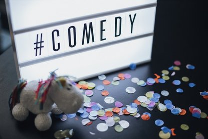 Auf einer Leuchtbox steht "Comedy", buntes Konfetti und ein gehäkeltes Einhorn liegt davor