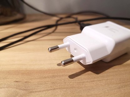 Weißer Stecker von Ladekabel liegt auf Holztisch