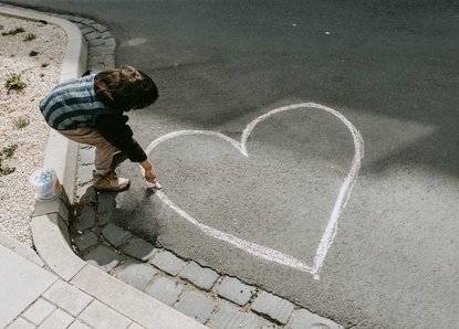 Junge malt mit Kreide ein Herz auf die Straße
