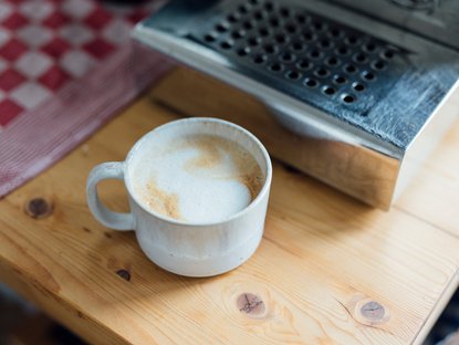Tasse mit Cappuccino steht auf Arbeitsplatte.