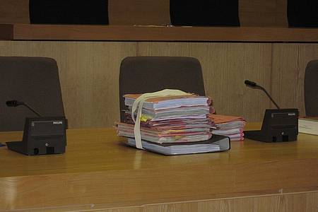Tisch im Gerichtssaal dahinter zwei Stühle auf dem Tisch eine rote dicke Aktenmappe