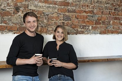 CHRISSI&MADLINE stehen mit einem Kaffee in der Hand nebeneinander