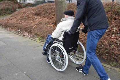 Mann schiebt anderen Mann im Rollstuhl