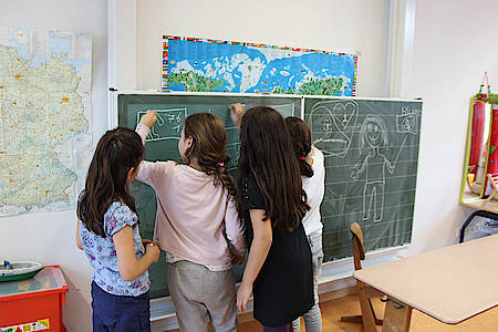 Kinder malen mit Kreide an die Schultafel