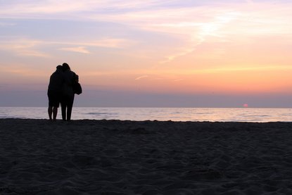 Paar steht am Meer und schaut auf einen Sonnenuntergang