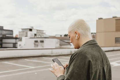 Frau mit kurzen Haaren steht auf Parkplatz und tippt auf dem Handy