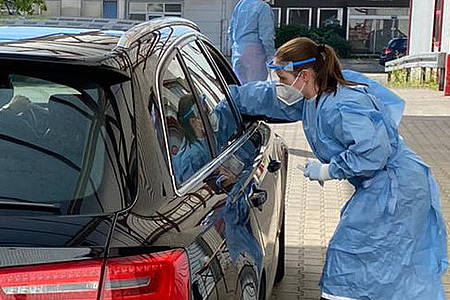 Ein Mitarbeiter des Testzentrums lehnt sich durch die Seitenscheibe eines Autos und führt ein Wattestäbchen in die Nase einer Testperson ein