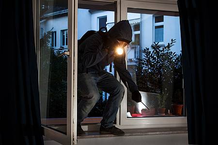 Einbrecher mit Taschenlampe steigt durch ein Fenster