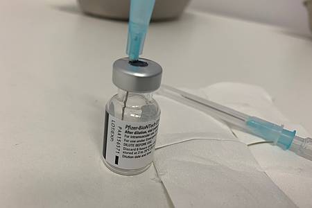 Eine Spritzennadel steckt in einer angebrochenen Ampulle von BioNTech 